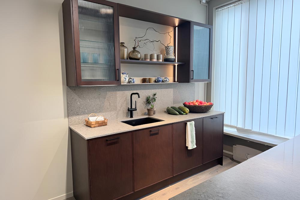 Kompakt modern köksbänk i trä med stenbänkskiva, mindre handfat, underskåp och överskåp för förvaring med en öppen hylla.